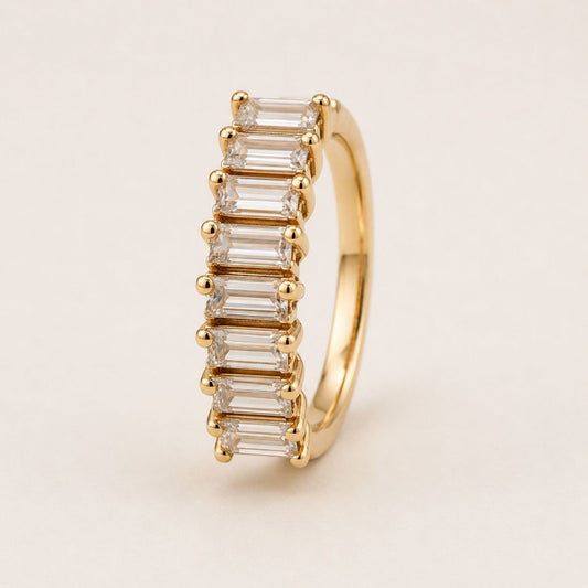 Gold ring with emerald-cut diamonds on a beige background